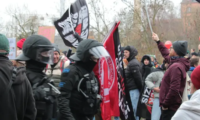 Demonstranten mit Fahnen, darunter eine mit der Aufschrift "System Metternich", und Polizisten in Schutzkleidung.