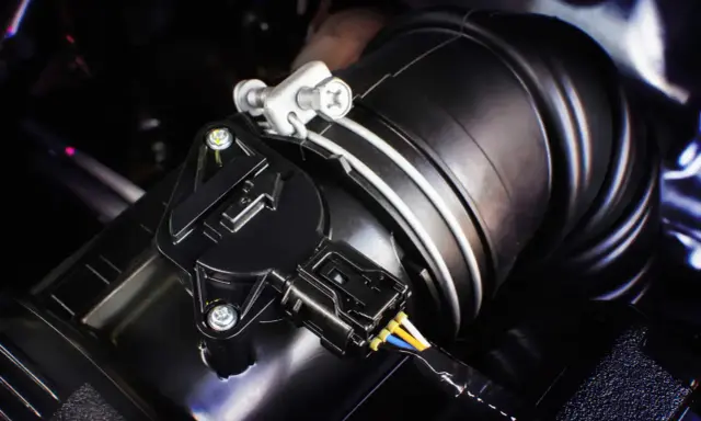 Detalle de un sensor MAF negro conectado a un tubo de admisión de aire. Este componente es clave para saber qué es el sensor MAF y cómo optimiza el rendimiento del motor.