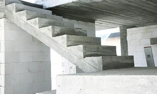 Surowe, betonowe schody czekają na wykończenie. W tle białe bloczki budowlane.