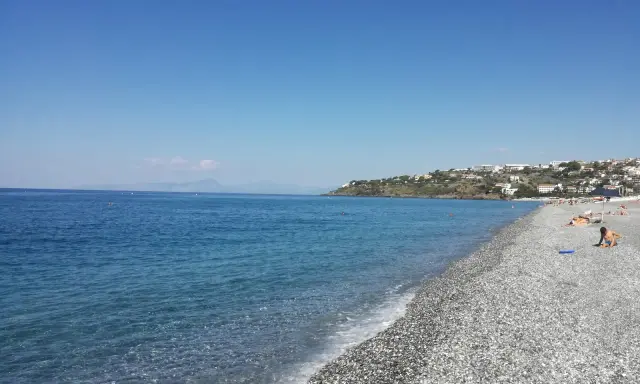 Spiaggia di ciottoli con mare azzurro e case arroccate sulla collina. Una giornata perfetta per godersi la **scalinea mare**.