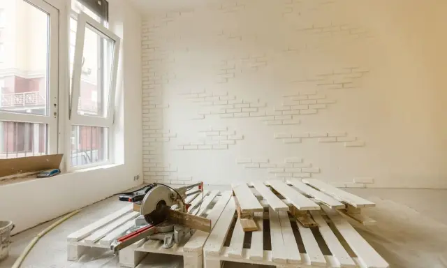 Herramientas listas para como pintar un palet. Madera blanca apilada, sierra ingletadora y pared con ladrillos blancos.