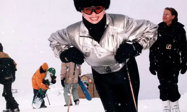 Ivana Trump joven, sonriendo y esquiando con un gorro de piel y gafas de esquí. A su alrededor, otras personas disfrutan de la nieve.