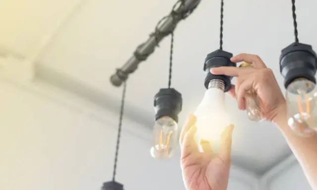Main d'une personne installant une ampoule gradable dans un lustre.