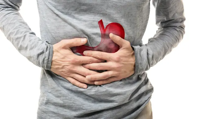 Uomo con mani sullo stomaco, dove un'immagine rossa evidenzia un possibile tumore allo stomaco.
