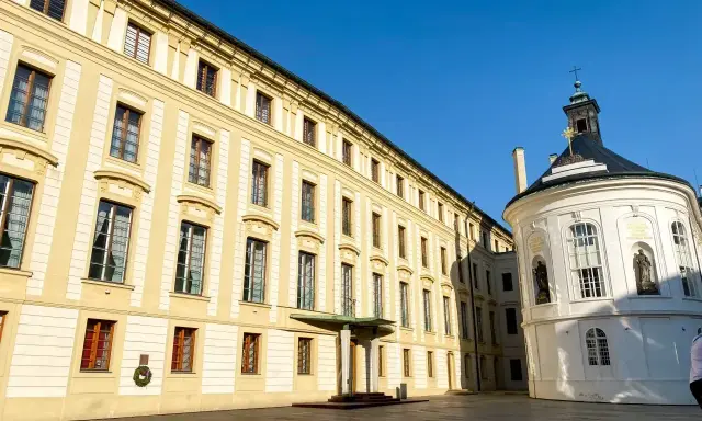 Zamek na Hradczanach, z jego długą, kremową fasadą i okrągłą, białą kaplicą, prezentuje się majestatycznie pod błękitnym niebem.