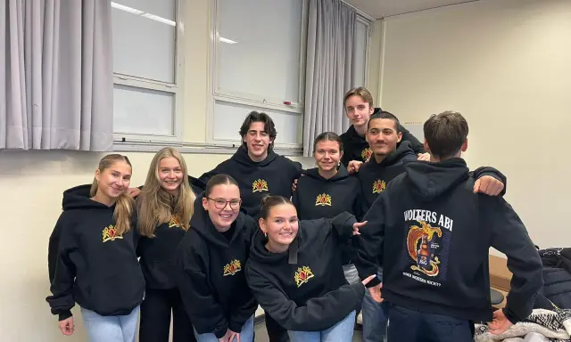 Acht lächelnde Schüler in schwarzen Hoodies mit dem Aufdruck "Volters Abi". Wie nennt man das Abitur noch?