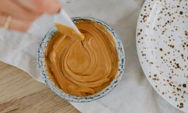 Une spatule prélève une portion de crème d'amandes légère dans un bol. Une assiette tachetée est à côté.