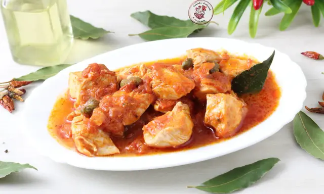 Succulento pollo alla pizzaiola con pomodoro, capperi e olive, guarnito con foglie di alloro e peperoncini secchi.