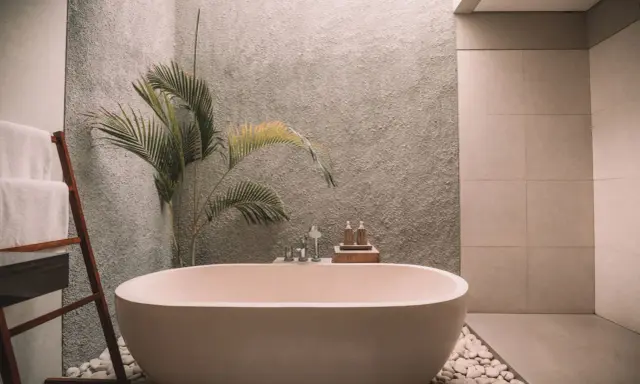Relajante bañera exenta rodeada de piedras blancas, toallas dobladas en una escalera de madera y una planta tropical. Un ejemplo de cuartos de baño modernos y serenos.