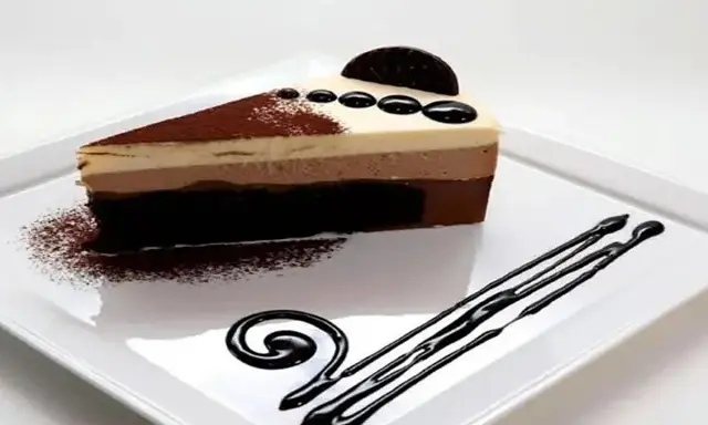 Una rebanada de tarta de tres chocolates, con capas de mousse de chocolate blanco, con leche y negro, espolvoreada con cacao y decorada con chocolate.
