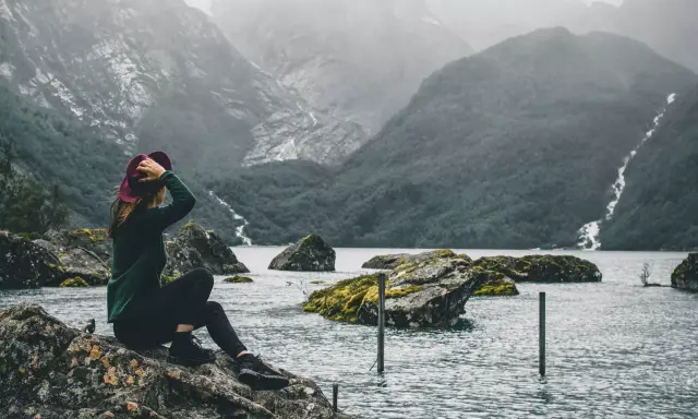 Kobieta w kapeluszu podziwia surowe piękno norweskiej przyrody. Woda, góry i wodospad tworzą malowniczy krajobraz, który oddaje esencję życia w Norwegii.