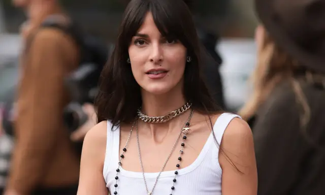 Frau mit langen Haaren und Curtain Bangs, trägt weiße Tanktop und Chanel-Schmuck.