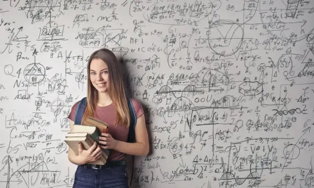 Uśmiechnięta studentka z książkami przed ścianą pełną równań matematycznych. Zastanawia się, co po studiach matematycznych.