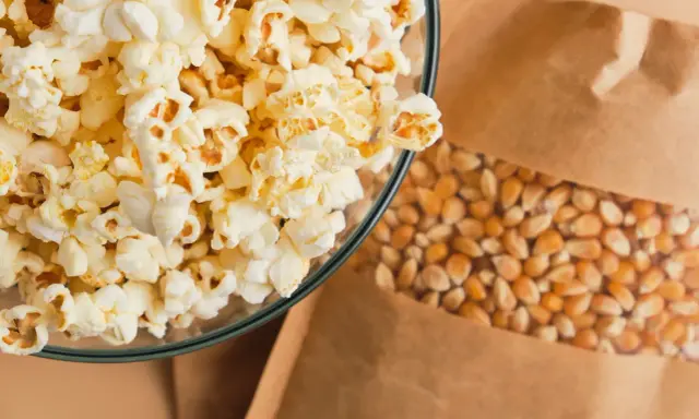 Miseczka pełna puszystego popcornu obok woreczka z ziarnami kukurydzy. Czy popcorn jest lekkostrawny? Zależy od dodatków!