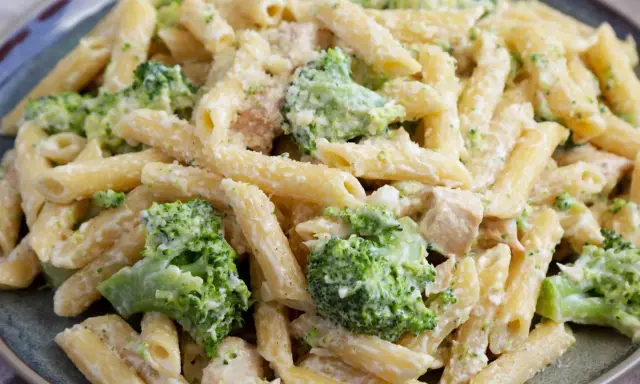 Penne z kurczakiem i brokułami w kremowym sosie, posypane parmezanem. Pyszny makaron z brokułami na talerzu.