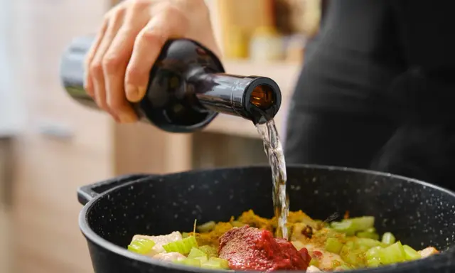 Una mano vierte vino en una sartén con ingredientes. El vino en moderación realza el sabor de la comida.