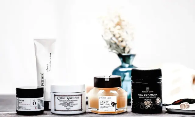 Plusieurs masques pour le visage, dont un masque au miel, sont disposés sur une table en bois.