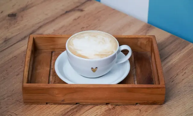 Eine Tasse Kaffee au lait mit Herz-Detail auf einem Holzteller, bereit zum Genießen.