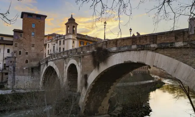 El puente Fabricio, con sus arcos de piedra y la torre medieval, cruza el Tíber bajo un cielo anaranjado.