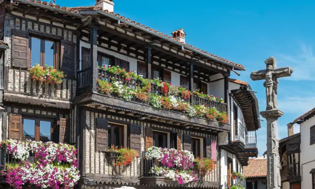 Casas de madera y piedra adornadas con flores en la Sierra de Francia. Un crucero de piedra se alza en la plaza.