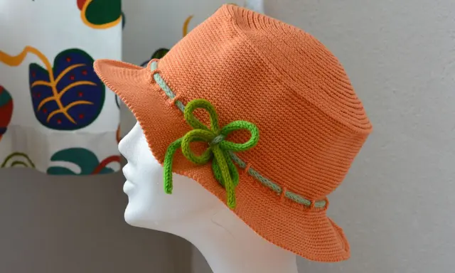 En orange virkad hatt med ljusgröna detaljer och en rosett. Perfekt för sommaren!