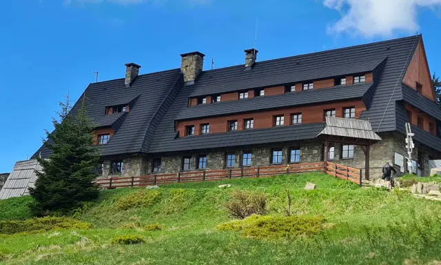 Schronisko na Turbaczu, cel wielu tras rowerowych i pieszych. Kamienno-drewniany budynek na zielonym wzgórzu.