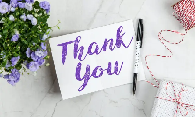 Carte "Thank You" violette, entourée de fleurs bleues, d'un stylo étoilé et d'un cadeau emballé. Une belle façon de remercier quelqu'un pour sa gentillesse.