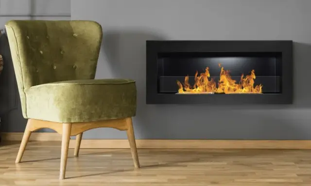 Sillón verde junto a chimenea moderna encendida. Un ejemplo de como encender la chimenea para crear un ambiente acogedor.