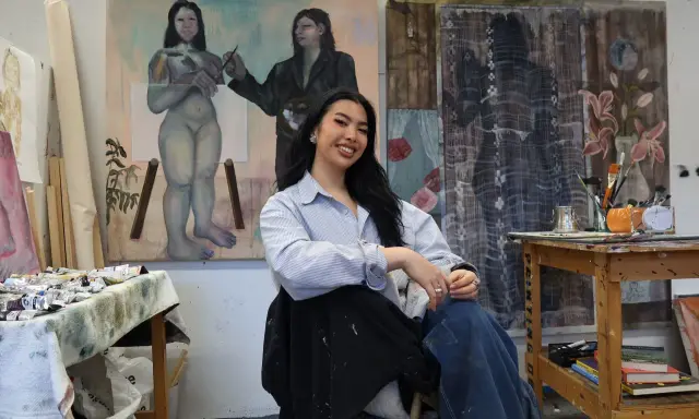 A young woman, one of many talented gen z artists, smiles in her studio, surrounded by her evocative paintings.