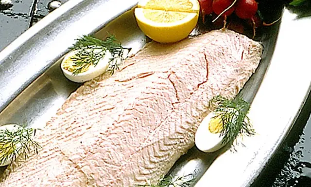 En vacker inkokt lax serveras på ett silverfat med citronklyftor, kokta ägg och dill.
