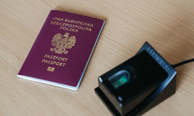 Polski paszport i czytnik linii papilarnych na drewnianym blacie.