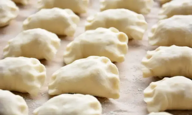 Gotowe do gotowania ciasto na pierogi, ułożone rzędami na blacie.