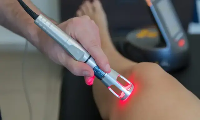 Fizjoterapeuta wykonuje laser zabieg rehabilitacyjny na kolanie pacjenta.