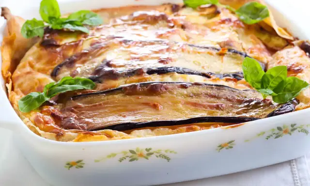 Parmigiana di melanzane napoletana recién horneada, dorada y burbujeante, decorada con hojas de albahaca fresca.