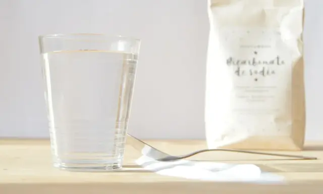 Un vaso de agua, una cuchara con bicarbonato y una bolsa de bicarbonato de sodio. ¡Listo para mezclar con vinagre!