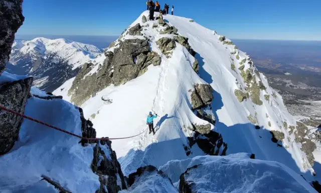 Grupa turystów na ośnieżonym szczycie. Widok na zimowe Tatry dla średniozaawansowanych.