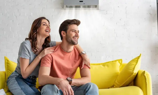 Couple souriant sur un canapé jaune, profitant de la brise fraîche d'un climatiseur moins de 50 db.