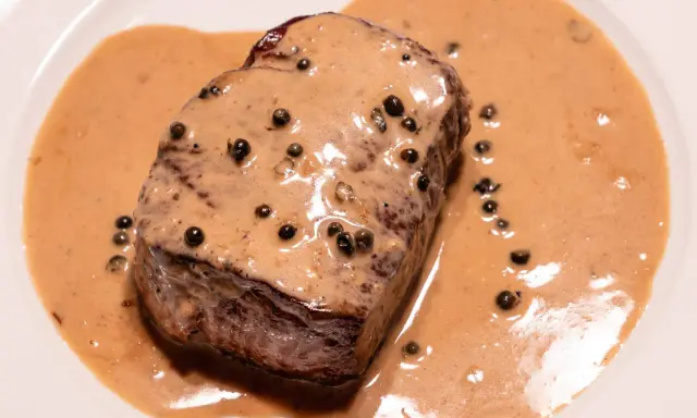 Un steak tendre baignant dans une onctueuse sauce au poivre, parsemée de grains de poivre noir. Un délice pour les yeux et les papilles.