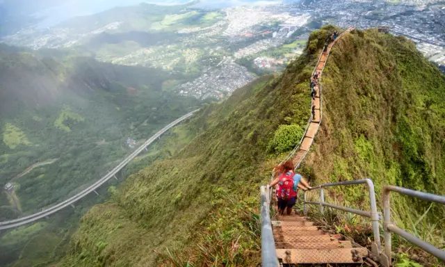 Wanderer erklimmen die "Stairway to Heaven" in Hawaii, eine steile Treppe mit atemberaubendem Blick auf die Stadt und die Natur.
