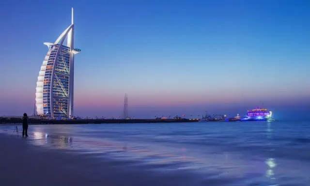 Wieczór w Dubaju. Luksusowy hotel Burdż al-Arab i oświetlony statek na morzu. Ceny w Dubaju mogą być wysokie, ale widoki są niezapomniane.