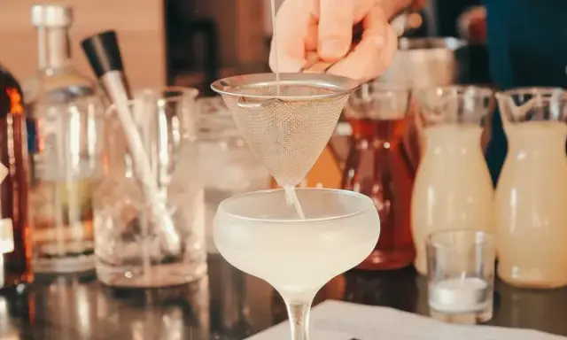 Ile napojów na wesele 80 osób? Barman przygotowuje drinka, w tle butelki z alkoholami i syropami.