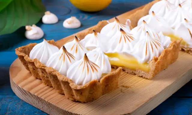 Tarta de limón con abundante merengue suizo tostado, sobre una tabla de madera.