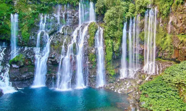 Vackra vattenfall kaskaderar nerför klippor täckta av frodig grönska, ner i en turkos lagun. En idyllisk plats nära Saint-Denis.
