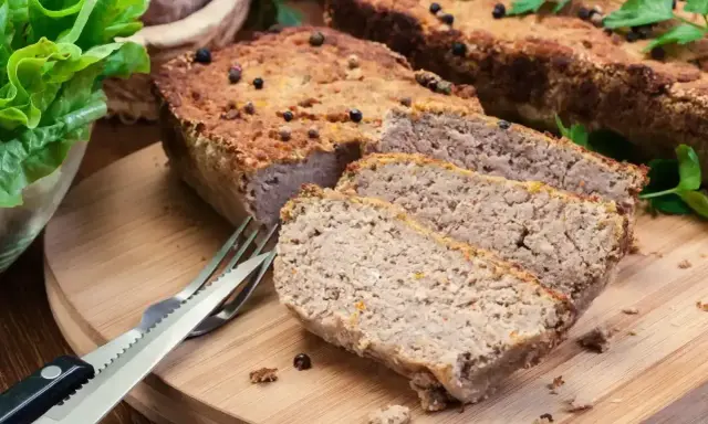 Domowy pasztet, idealny do pieczenia w temperaturze 180°C, pokrojony na desce z widelcem i sałatą.