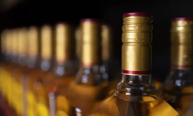 Rząd butelek z alkoholem, z złotymi zakrętkami. Czy to zapasy przed podróżą do Hiszpanii, gdzie obowiązuje limit alkoholu?