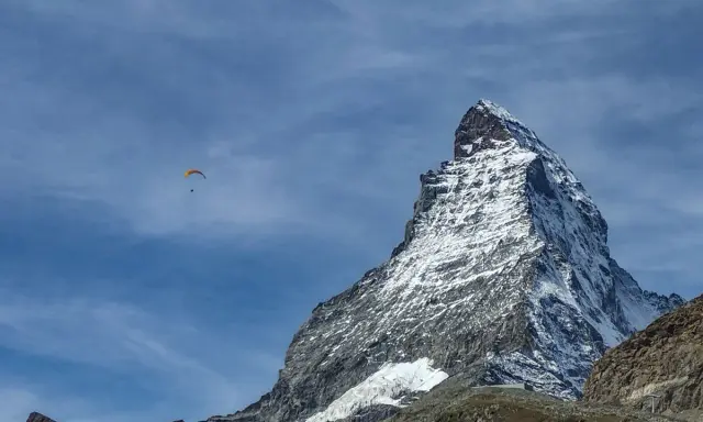 Majestatyczny polski Matterhorn, pokryty śniegiem, góruje nad krajobrazem. Na błękitnym niebie, wśród chmur, szybujący paralotniarz.