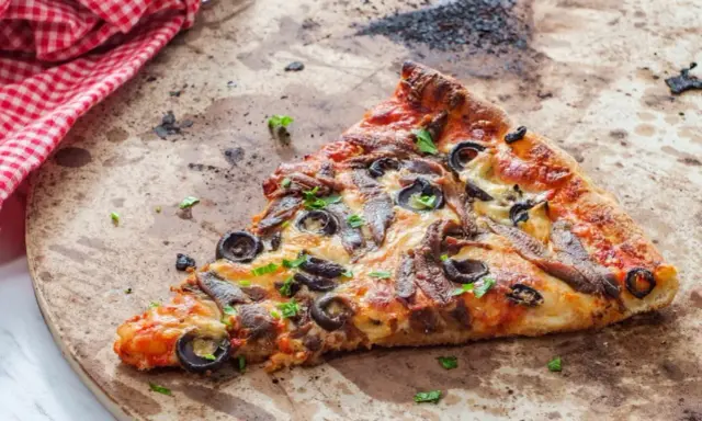 Une part de pizza aux anchois et olives sur une pierre réfractaire, prête pour un nettoyage.