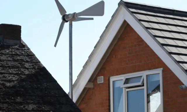 Une petite éolienne maison capte le vent au-dessus des toits.