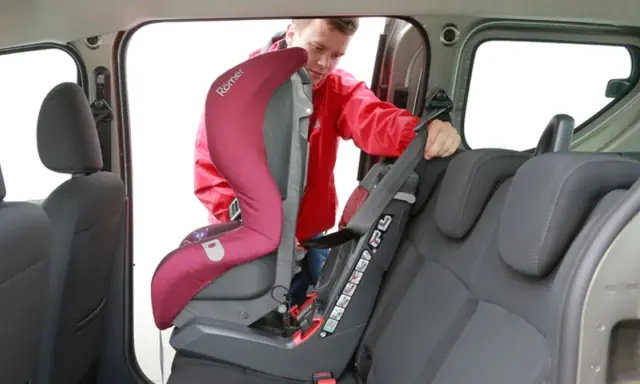 Mężczyzna montuje fotelik samochodowy. Sprawdź, jak sprawdzić, czy samochód ma isofix, patrząc na zaczepy fotelika.