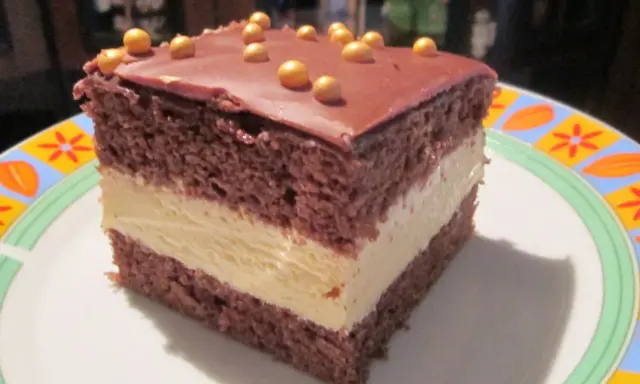 Pyszne milky way ciasto z czekoladowym blatem i kremowym nadzieniem, ozdobione złotymi kuleczkami.